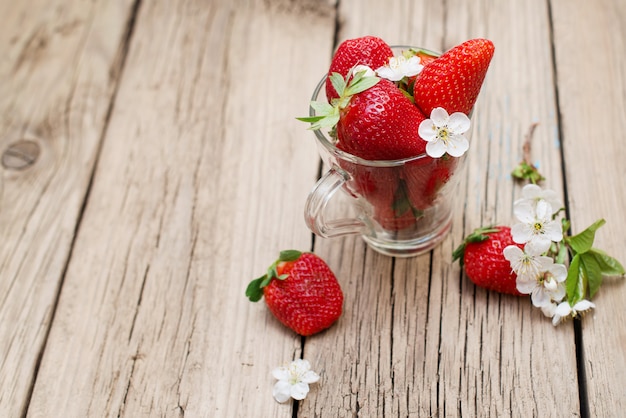 Fragole fresche in una tazza di vetro su una tavola di legno