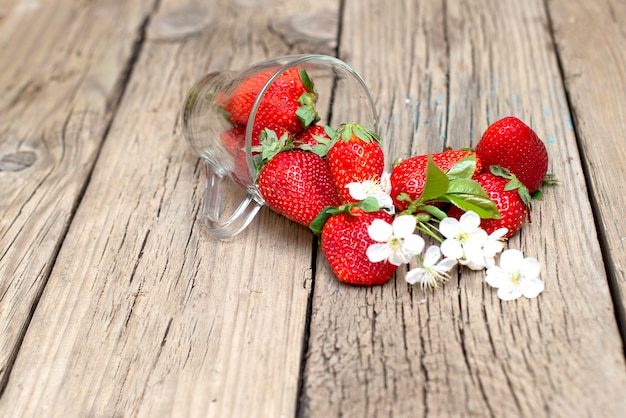 Fragole fresche in una tazza di vetro su una tavola di legno