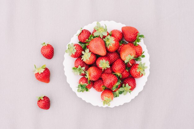 Fragole fresche su una zolla bianca, illuminata dal sole luminoso. La superficie grigia. Lay piatto.