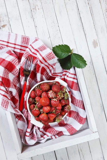 Fragole fresche succose sul piatto bianco in scatola di legno.