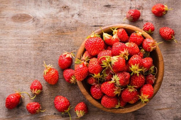 Fragole in una ciotola di legno e intorno su una tavola di legno. Vista dall'alto