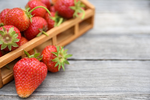 Fragole in una ciotola su una tavola di legno, all'aperto su una natura vaga verde delle foglie e degli alberi