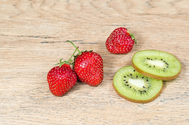 Fragole mature e fette di kiwi giacciono su un vecchio tavolo di legno, primo piano