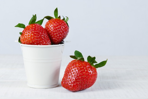 Fragole mature fresche in un piccolo secchio bianco su un tavolo di legno bianco