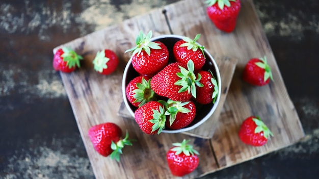 Fragole mature fresche in una ciotola e su una superficie di legno.