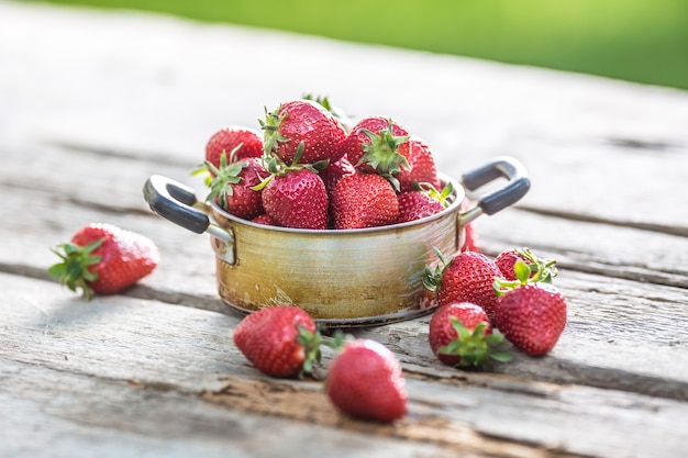 Fragole mature fresche in vaso da cucina vintage sul vecchio tavolo da giardino.