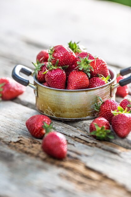 Fragole mature fresche in vaso da cucina vintage sul vecchio tavolo da giardino.