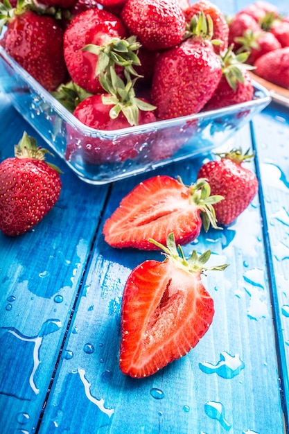 Fragole mature fresche lavate con acqua sul tavolo blu.