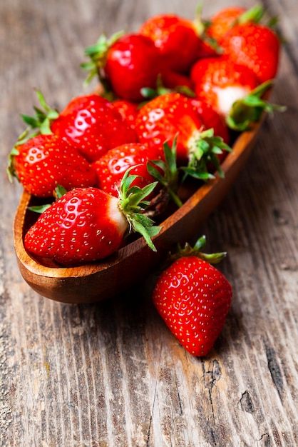 Fragole mature in una ciotola di legno su uno sfondo di legno.