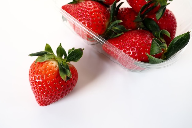 Fragole mature in una confezione di plastica su sfondo bianco Deliziose bacche fresche in un contenitore per la vendita ai clienti Mantenere il cibo fresco Cibo sano Una fragola estratta dal contenitore