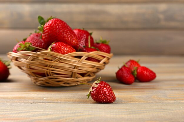 Fragole mature rosse in cestino di vimini su fondo di legno