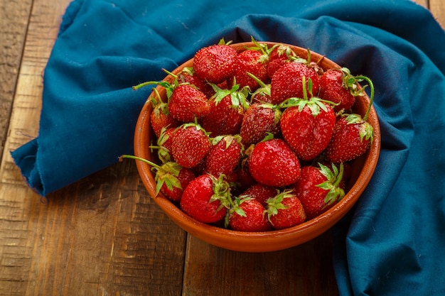 Fragole mature su un piatto di argilla su uno sfondo di legno