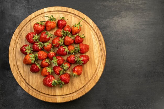 Fragole mature sul vassoio di legno su fondo nero. Vista dall'alto. Fragole dolci fatte in casa.