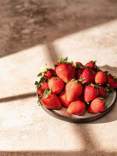 Fragole nel piatto su fondo strutturato marrone con lo spazio della copia delle ombre della finestra