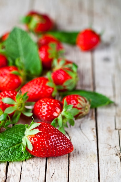 Fragole rosse fresche e foglie di menta su fondo di legno rustico.