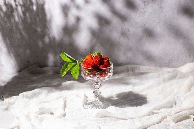 Fragole rosse fresche in un bicchiere all'ombra dei fiori su un tavolo su uno sfondo di cemento.