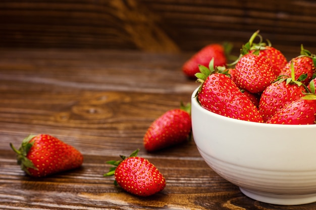 Fragole rosse in ciotola su un fondo di legno