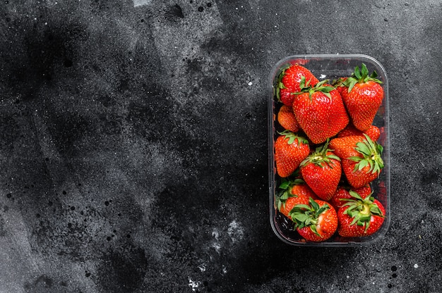 Fragole rosse mature nell'imballaggio di plastica sul nero. Vista dall'alto. Copia spazio