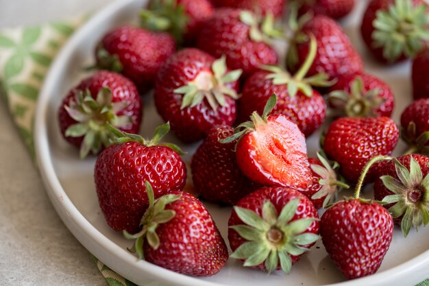 Fragole succose mature in un piatto di argilla su uno sfondo chiaro con spazio di copia