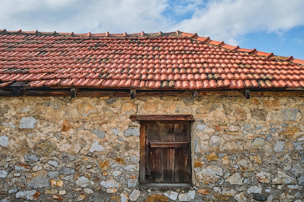 Frammento di un antico casale in pietra con persiane chiuse e tetto di tegole un'idea per lo sfondo o lo sfondo delle fattorie ecologiche