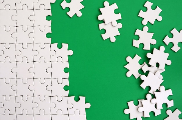 Frammento di un puzzle bianco piegato e un mucchio di elementi di puzzle non letti sullo sfondo di una superficie verde.