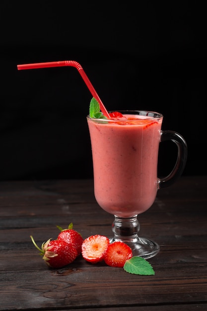 Frappè alla fragola fresca decorato con frutti di bosco su una parete scura, il concetto di una sana colazione, dieta e buona alimentazione.