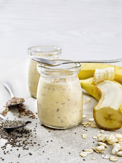 Frappè con semi di chia, semi di lino, farina d'avena, riso soffiato e banana in due vasetti di vetro su uno sfondo di tavolo in pietra