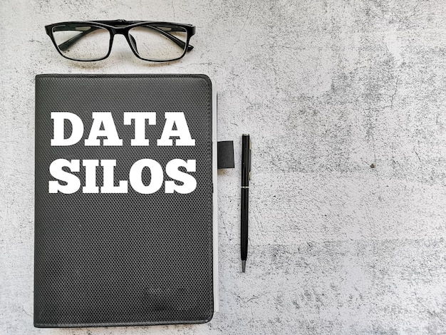 Frase Data Silos scritta su taccuino con penna e occhiali. Concetto di business e tecnologia.