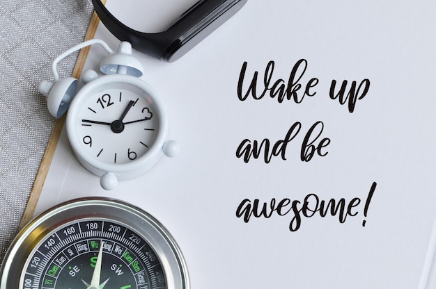 Frase WAKE UP AND BE AWESOME scritta su taccuino con orologio e bussola