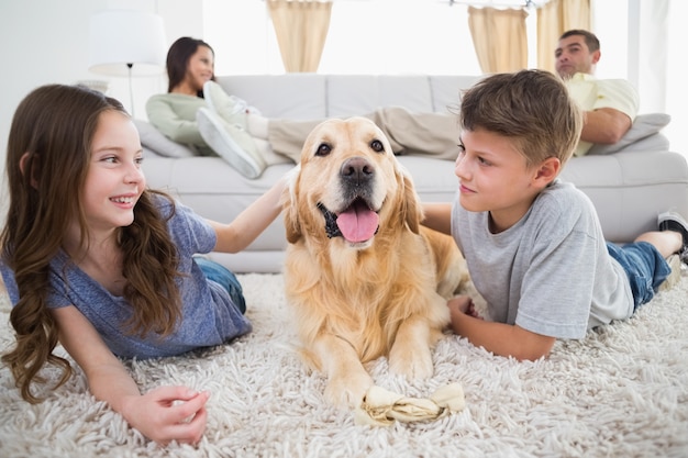 Fratelli germani accarezzando il cane sul tappeto mentre i genitori si rilassano sul divano