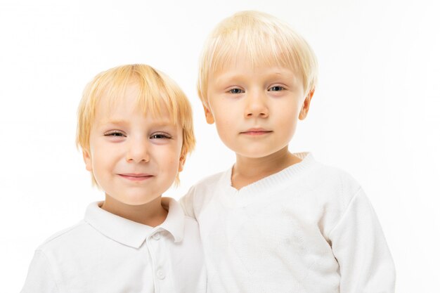 Fratelli piccoli con capelli corti e rossi, occhi azzurri, aspetto carino, in giacca bianca, pantaloni azzurri, alzati e posa magnificamente sulla fotocamera