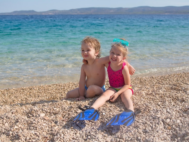 fratellini e sorelle carinissimi che si siedono sulla spiaggia e si abbracciano