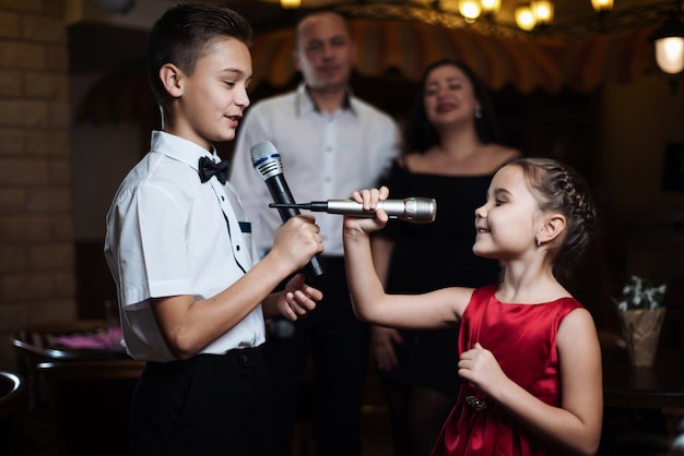 Fratello e sorella cantano canzoni di karaoke in microfoni e i loro genitori cantano nella parte posteriore