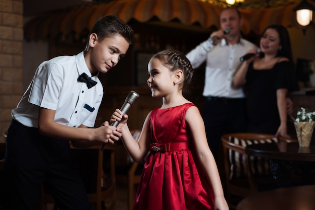 Fratello e sorella cantano canzoni per karaoke nei microfoni e i loro genitori cantano nella parte posteriore