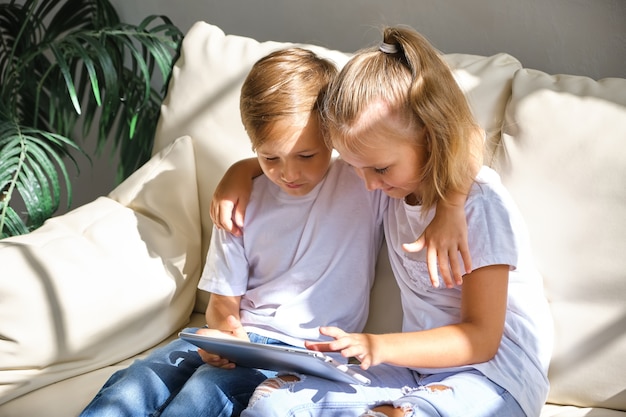 Fratello e sorella con computer tablet pc sul divano in soggiorno