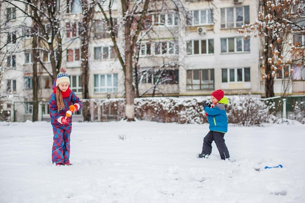 Fratello e sorella felici giocano a palle di neve durante una passeggiata invernale facendo palle di neve nel parco