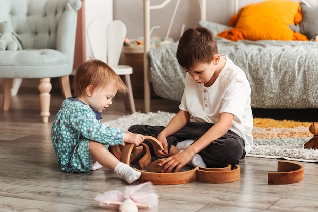 Fratello e sorella giocano con i giocattoli di legno nella stanza dei bambini. I bambini giocano con un designer di giocattoli sul pavimento.