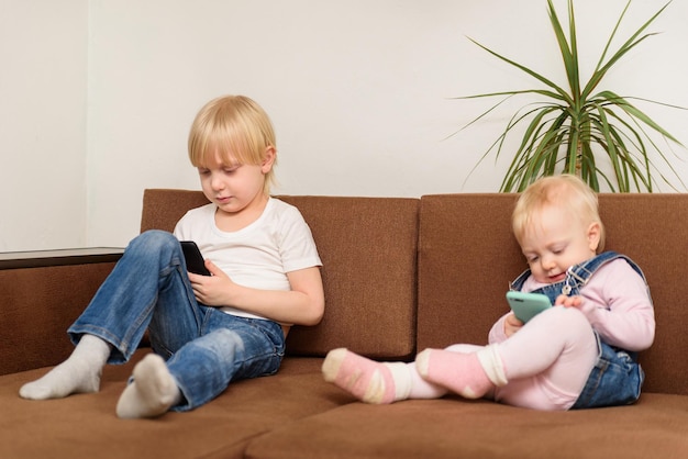 Fratello e sorella seduti sul divano guardando il telefono fratelli capelli biondi Concetto di generazione alfa