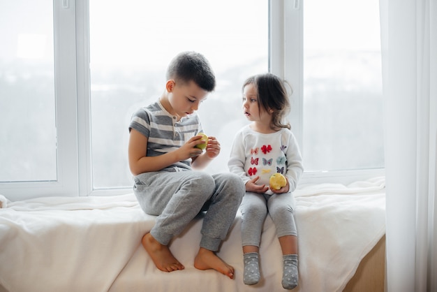 Fratello e sorella sono seduti sul davanzale a giocare e mangiare mele. Felicità