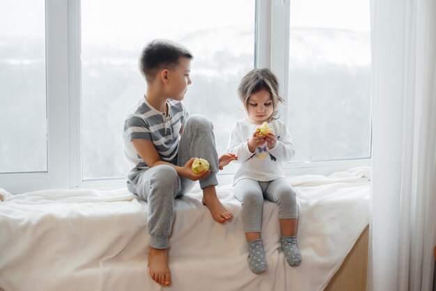 Fratello e sorella sono seduti sul davanzale a giocare e mangiare mele. Felicità