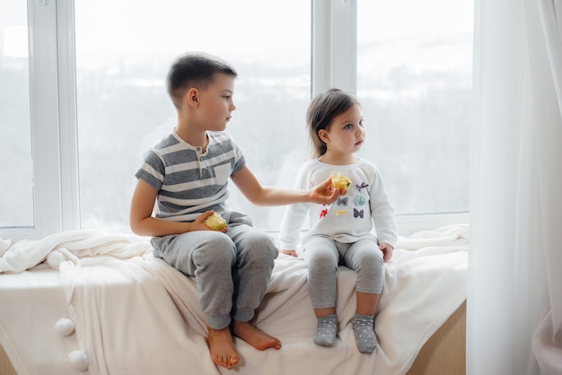 Fratello e sorella sono seduti sul davanzale a giocare e mangiare mele. Felicità