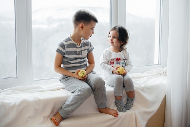 Fratello e sorella sono seduti sul davanzale a giocare e mangiare mele. Felicità