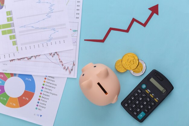 Freccia verso l'alto di crescita, grafici e tabelle, salvadanaio, monete e calcolatrice sull'azzurro. Successo aziendale