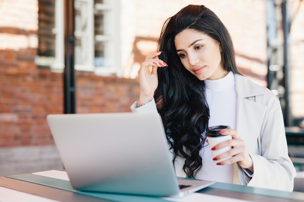 Free lance femminili europee che pensano alle idee per il suo nuovo progetto che lavora con il computer portatile mentre si siedono al self-service all'aperto