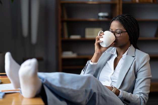 Freelancer donna afro rilassante sul posto di lavoro remoto con una tazza di tè benefici di lavorare da casa