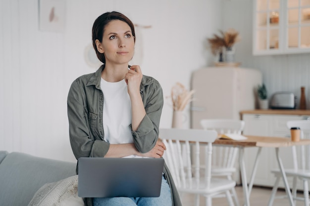 Freelancer sta pianificando il futuro e sognando una donna Spahish è seduta al computer in una cucina accogliente