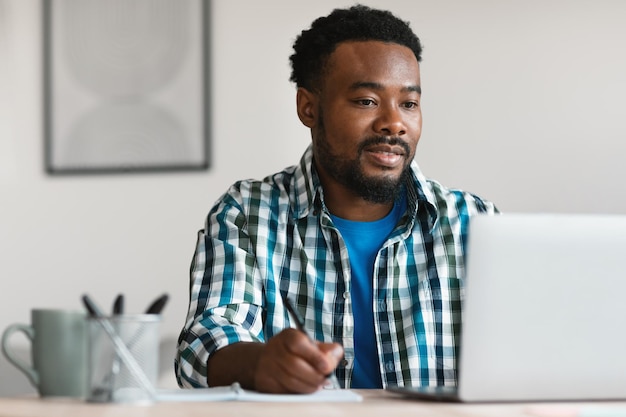 Freelancer uomo nero utilizzando laptop lavorando prendendo appunti sul posto di lavoro