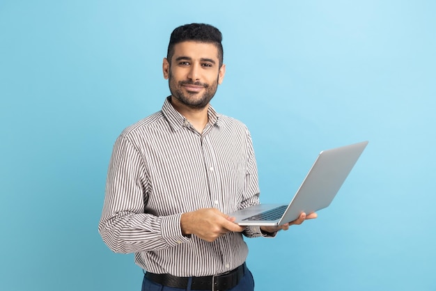 Freelancer uomo sorridente con la barba in piedi e tenendo il laptop soddisfatto del telelavoro