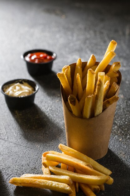 French Fries Bucket con salsa dip isolata su sfondo grigio scuro vista laterale del fast food