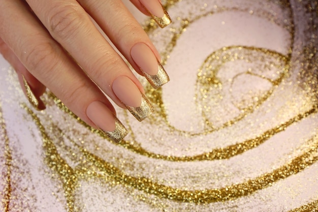 French manicure alla moda dorata su unghie lunghe con paillettes.